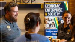 Three people standing around a presentation board with the words 'economy, enterprise, & society'