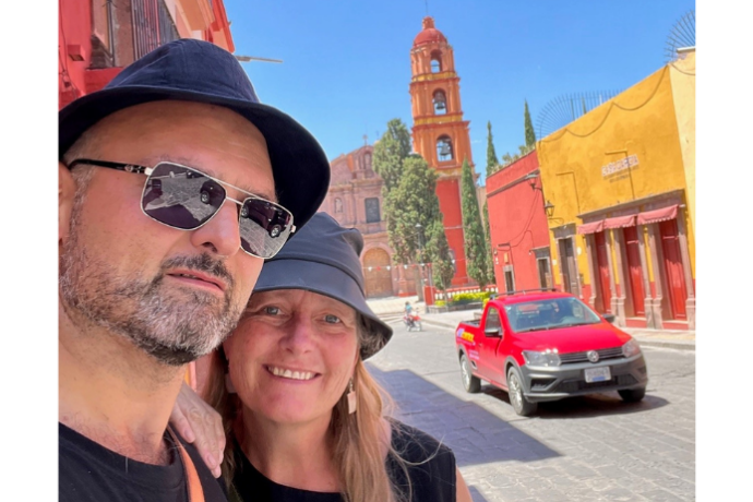 Marwan and Ute Kraidy stand in front of a cobblestone street with a red car and church steeple in the background.