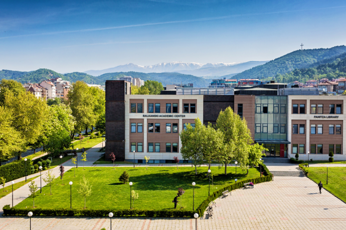 The outside of the Balkanski Academic Center at the American University in Bulgaria surrounded by bright green trees and faded blue mountains in the distance
