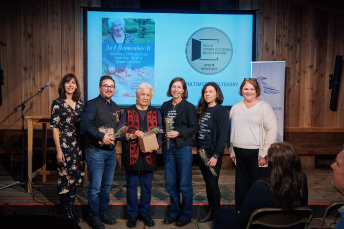 Six people stand in front of a screen with the ACLS Open Access book prize logo.