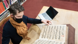 ACLS Fellow Aaron Hyman sits at a desk reading a book with musical notation at the Newberry Library.